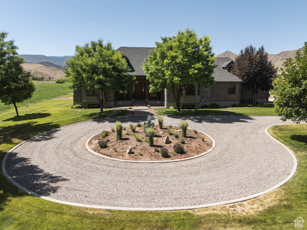 View of front facade with curved driveway, a front lawn, a mountain view, and a shingled roof