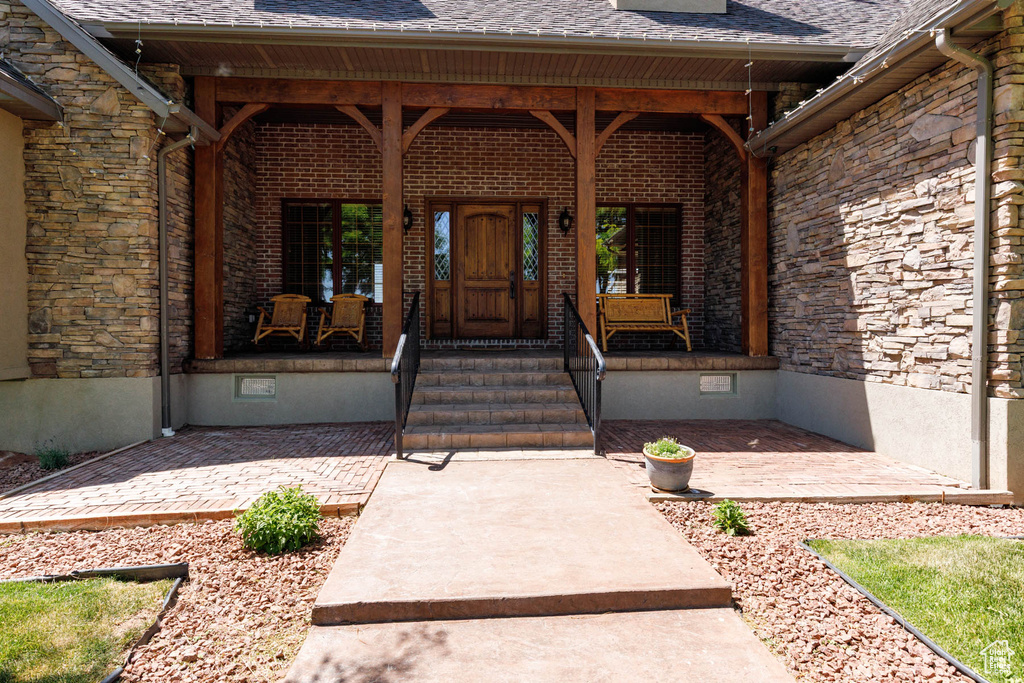 Property entrance with a porch, crawl space, a shingled roof, and stone siding
