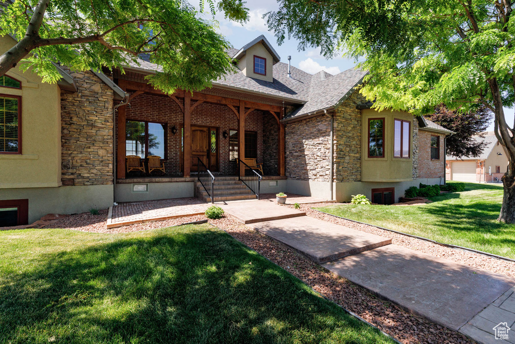 View of front of house with stone siding, a porch, a front lawn, and a shingled roof