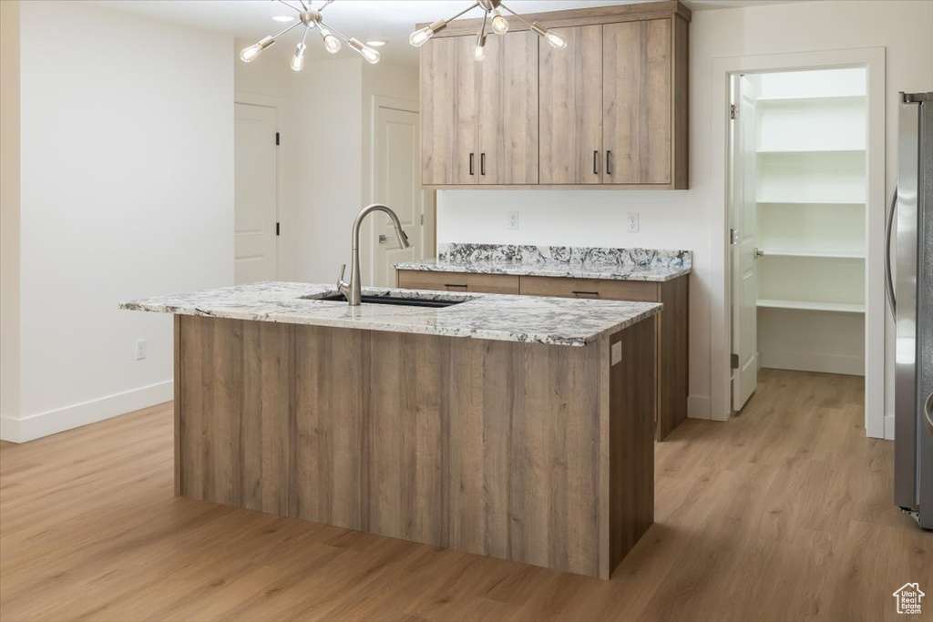 Kitchen with sink, an inviting chandelier, a center island with sink, light hardwood / wood-style flooring, and light stone countertops