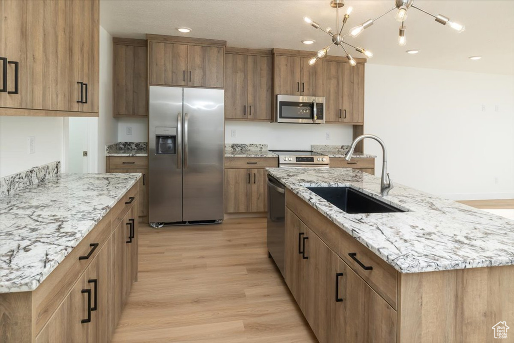 Kitchen with sink, a large island with sink, light stone counters, stainless steel appliances, and light wood-type flooring