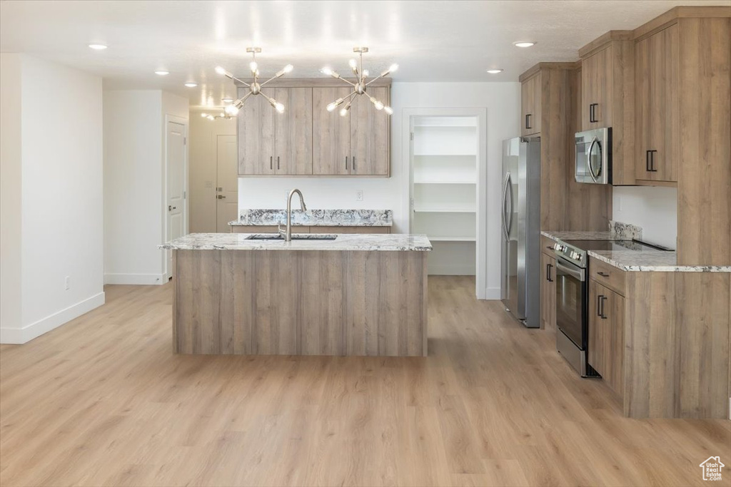 Kitchen featuring sink, an island with sink, pendant lighting, stainless steel appliances, and light stone countertops