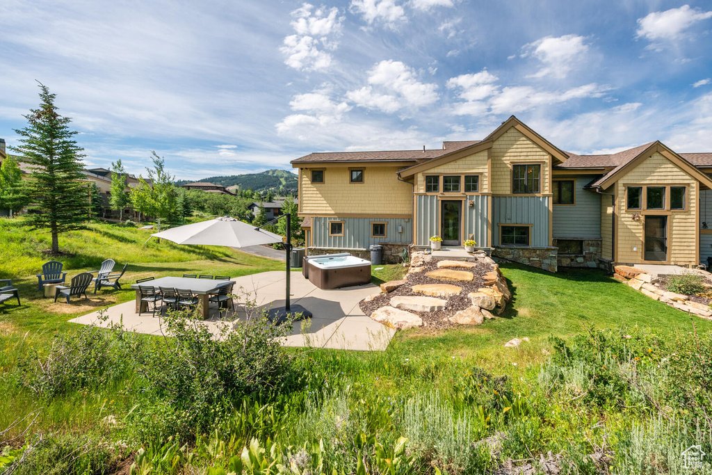 Rear view of house featuring a hot tub, a patio, and a lawn