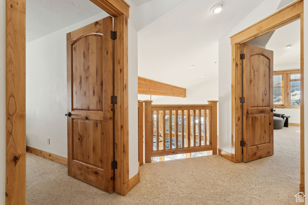 Hallway with vaulted ceiling and light colored carpet