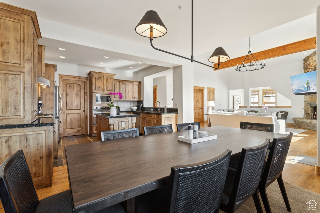 Dining area featuring sink, beam ceiling, an inviting chandelier, light wood-type flooring, and a fireplace