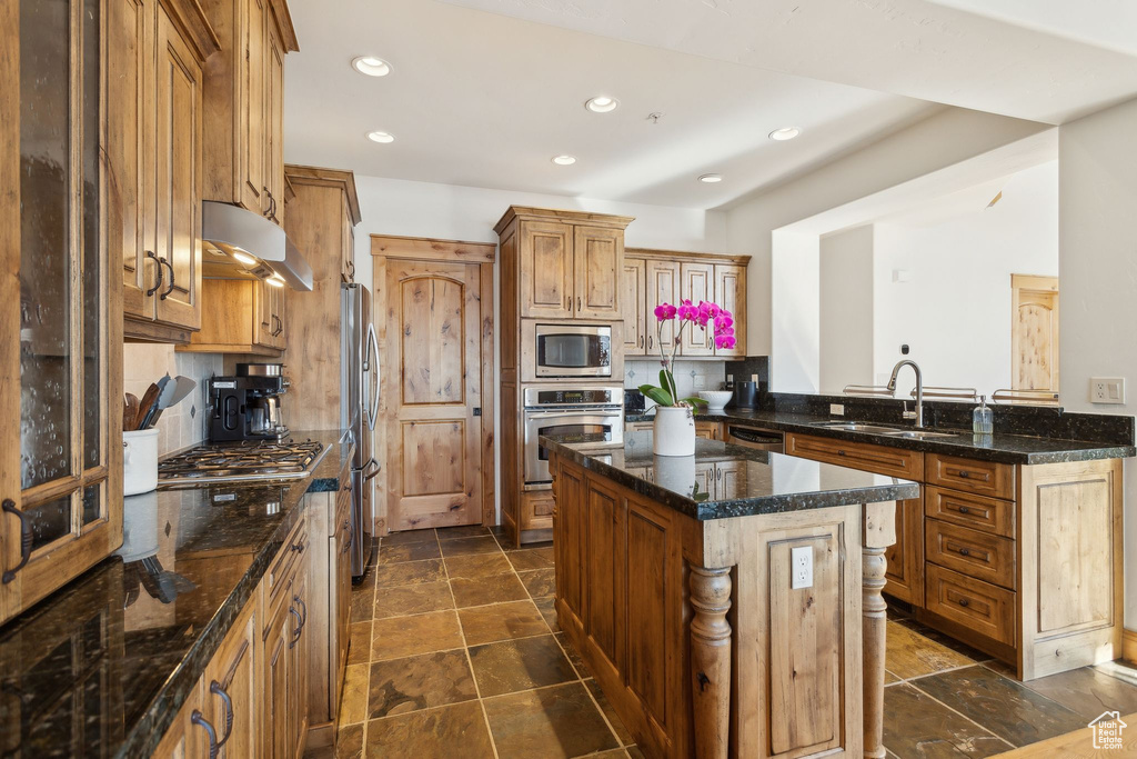 Kitchen with sink, appliances with stainless steel finishes, dark stone countertops, a kitchen island, and kitchen peninsula