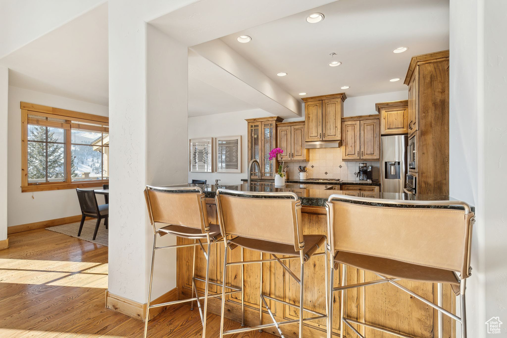 Kitchen with stainless steel fridge, a breakfast bar, backsplash, kitchen peninsula, and light wood-type flooring