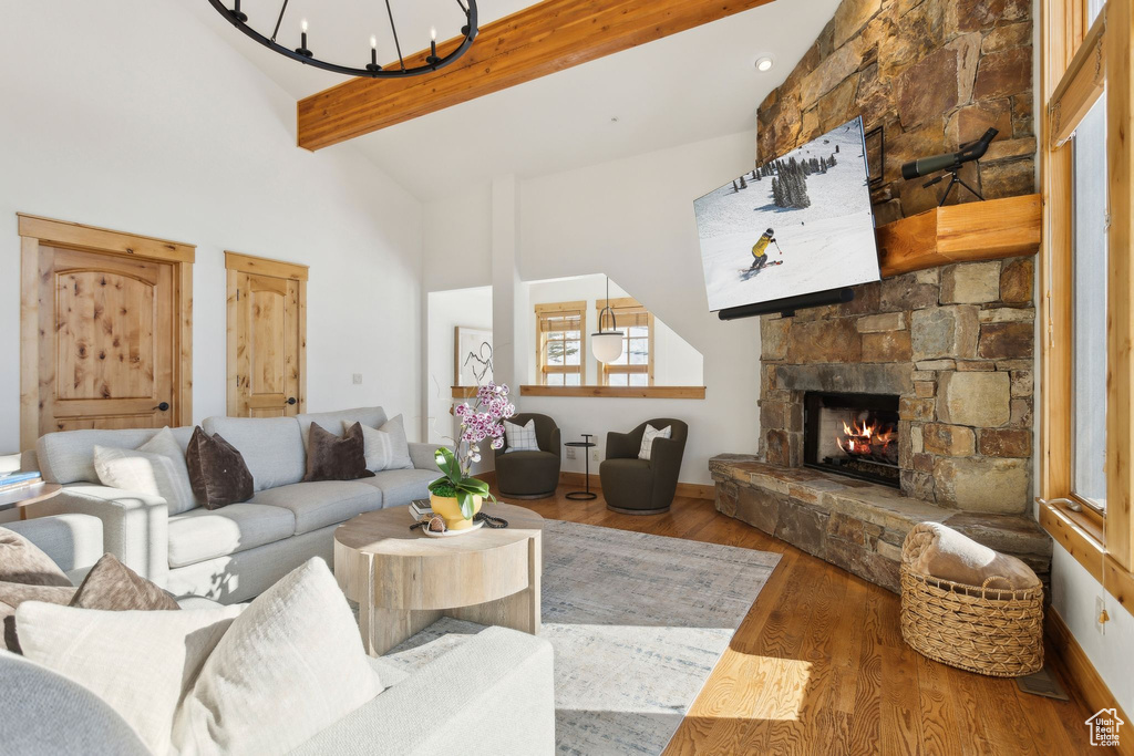 Living room featuring hardwood / wood-style flooring, a stone fireplace, high vaulted ceiling, and beamed ceiling