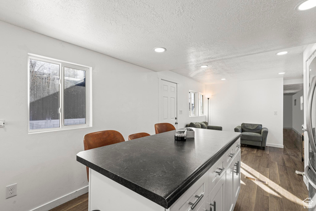 Kitchen with dark hardwood / wood-style flooring, a textured ceiling, white cabinets, and a kitchen island