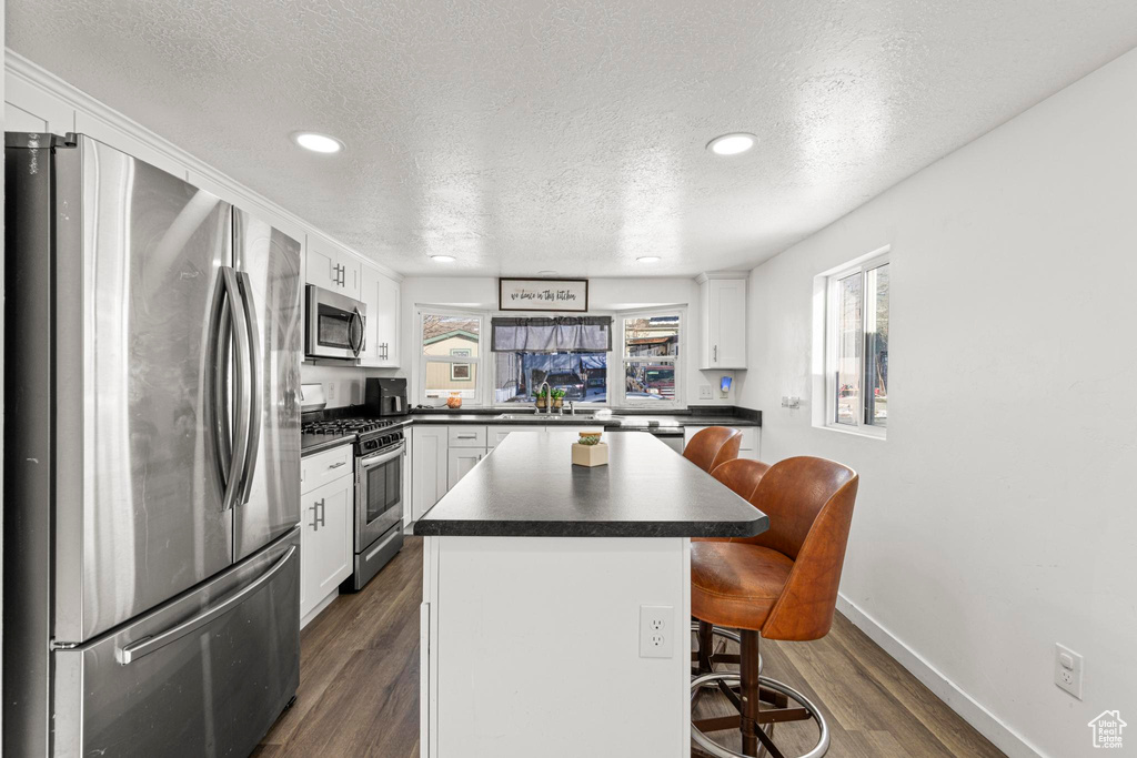 Kitchen featuring white cabinets, a kitchen bar, a center island, stainless steel appliances, and a textured ceiling