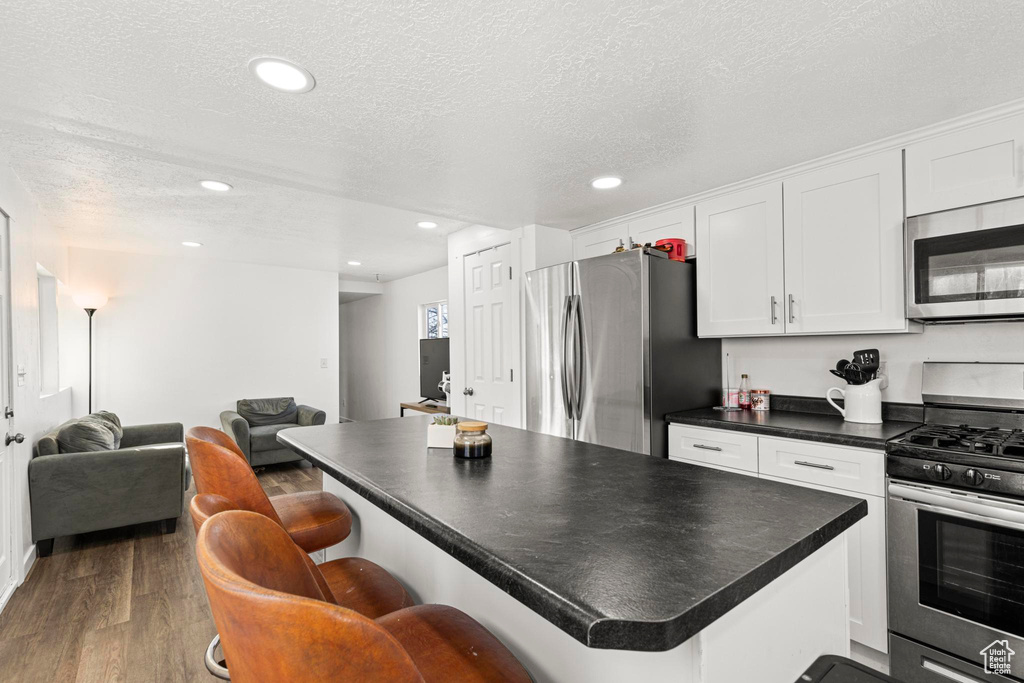 Kitchen featuring a kitchen bar, white cabinetry, a textured ceiling, appliances with stainless steel finishes, and dark hardwood / wood-style flooring