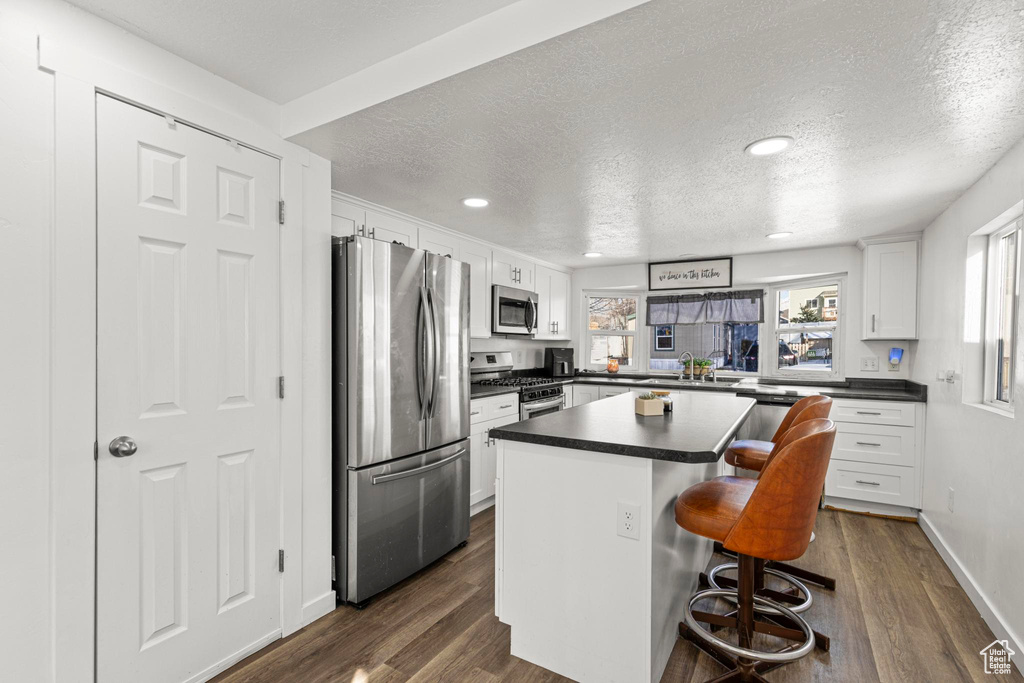 Kitchen featuring a kitchen island, appliances with stainless steel finishes, a breakfast bar area, white cabinets, and a textured ceiling