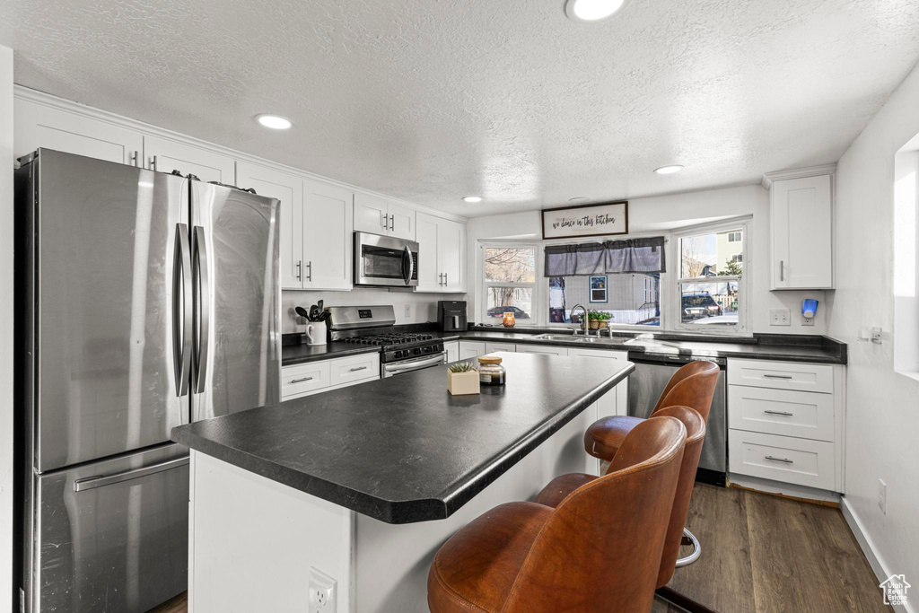 Kitchen with dark wood-type flooring, appliances with stainless steel finishes, white cabinetry, a center island, and a textured ceiling