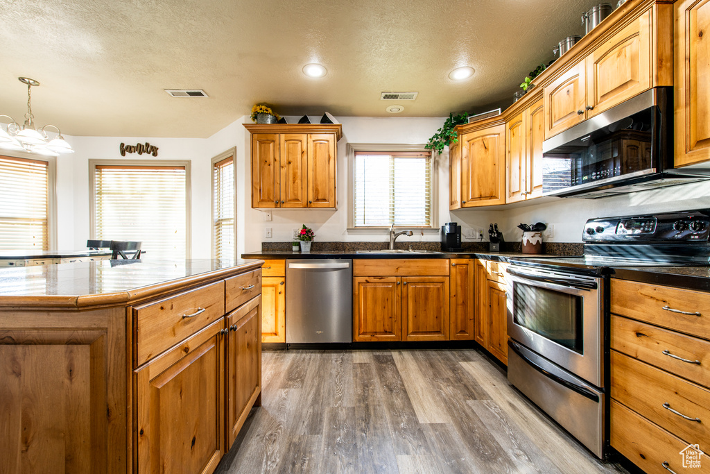 Kitchen featuring sink, appliances with stainless steel finishes, hardwood / wood-style floors, a textured ceiling, and decorative light fixtures