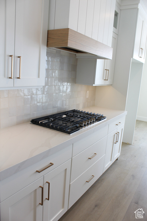 Kitchen with white cabinets, custom exhaust hood, gas stovetop, light stone countertops, and light hardwood / wood-style flooring