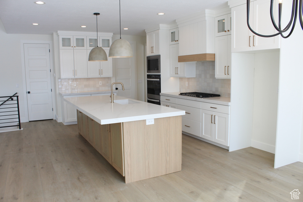 Kitchen with wall oven, a center island with sink, and white cabinets