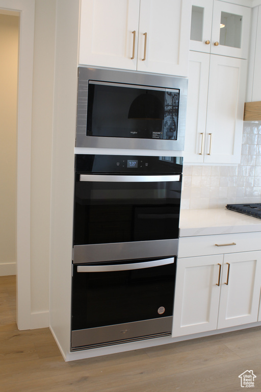 Details with black appliances, light hardwood / wood-style floors, decorative backsplash, and white cabinets