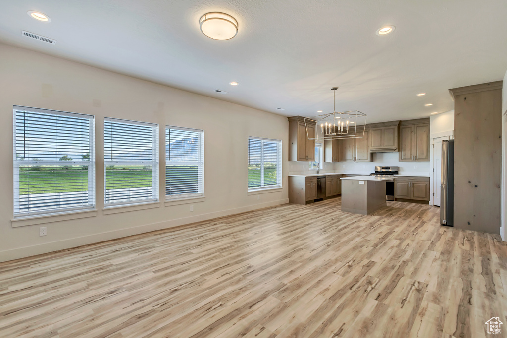 Kitchen with appliances with stainless steel finishes, a chandelier, a kitchen island, light countertops, and light wood-style flooring