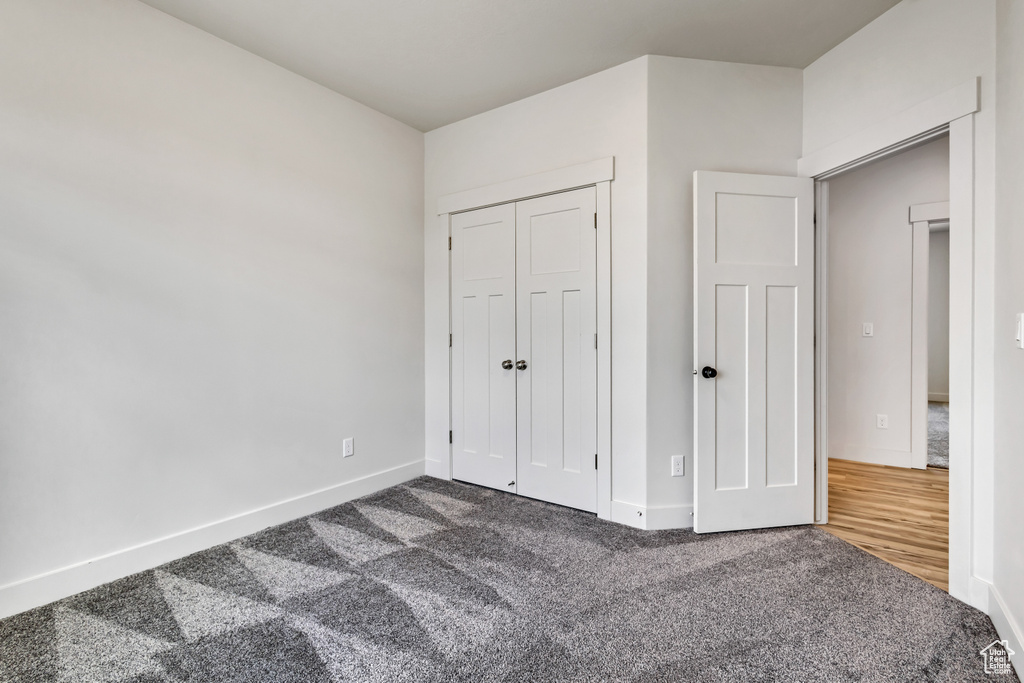Unfurnished bedroom with dark carpet, baseboards, and a closet