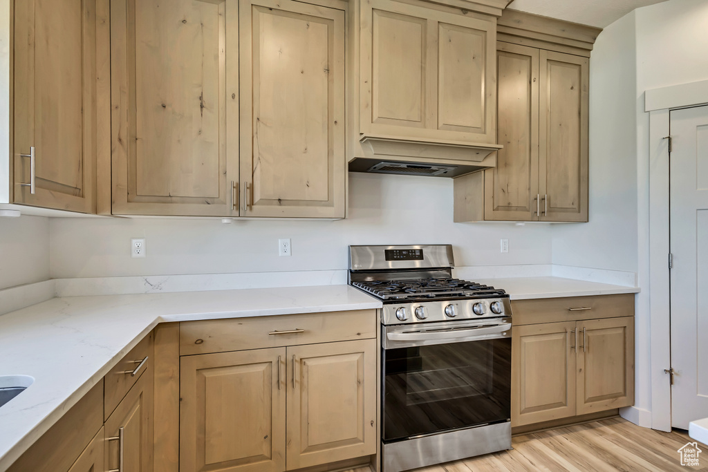 Kitchen featuring stainless steel gas stove, custom range hood, light stone countertops, and light wood-type flooring