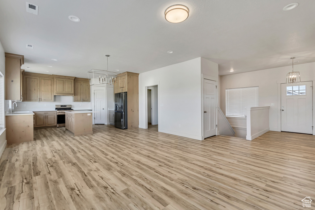 Kitchen with stainless steel stove, black refrigerator with ice dispenser, open floor plan, light countertops, and light wood-style flooring