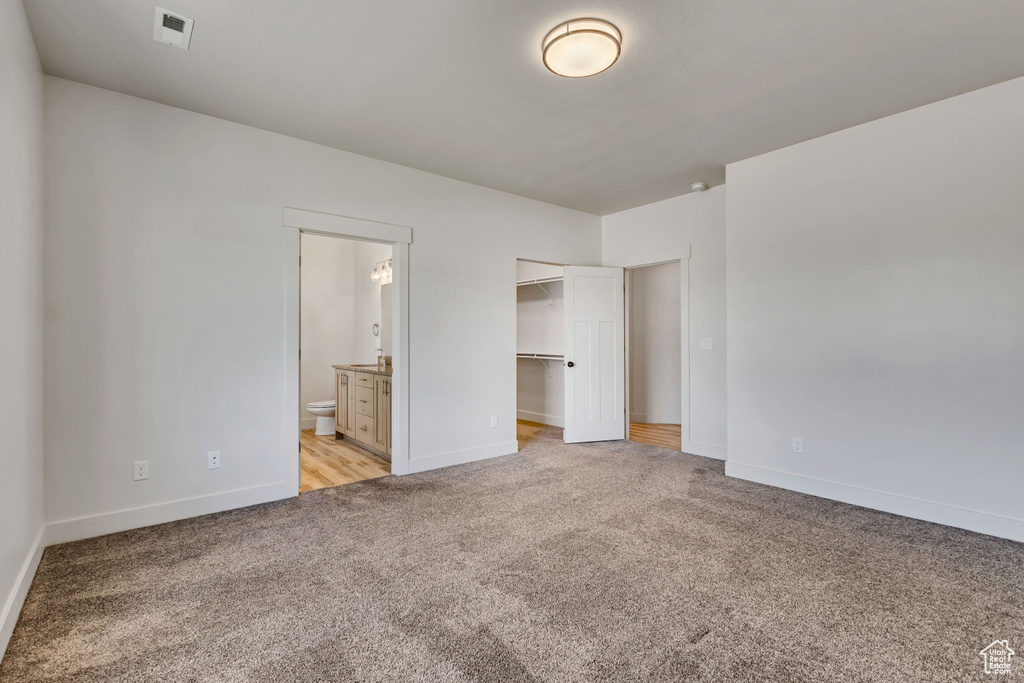 Unfurnished bedroom with light colored carpet, baseboards, connected bathroom, and a spacious closet