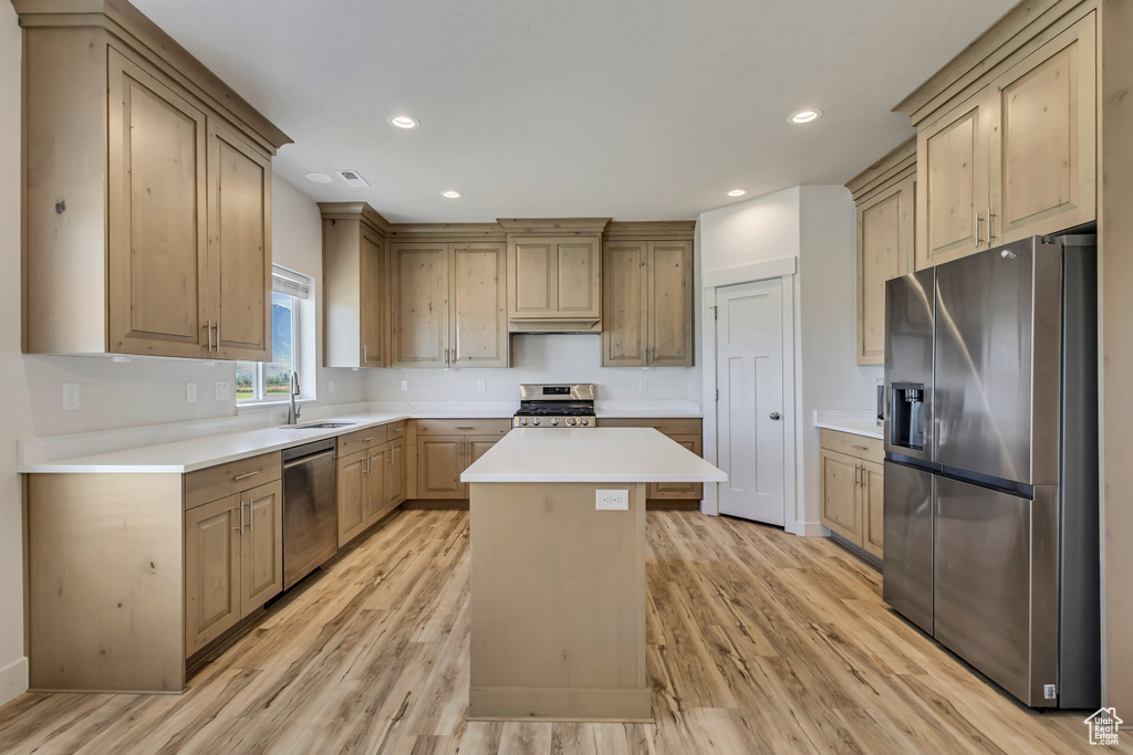 Kitchen with appliances with stainless steel finishes, a sink, light wood finished floors, a kitchen island, and recessed lighting