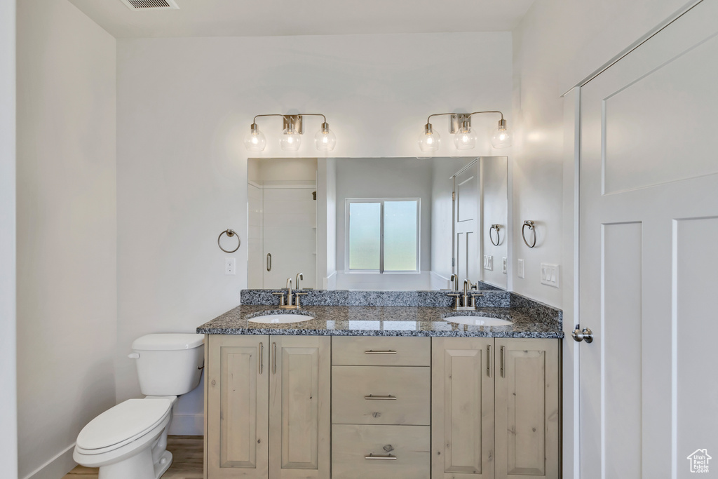 Bathroom featuring toilet, double vanity, a shower, and baseboards