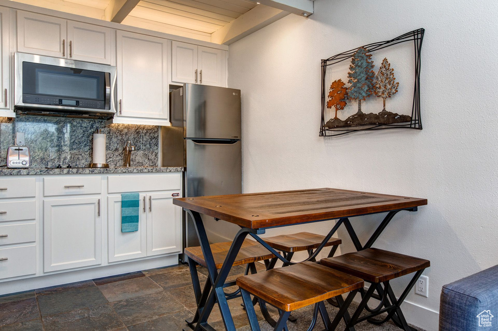 Kitchen featuring white cabinetry, backsplash, stone countertops, and appliances with stainless steel finishes