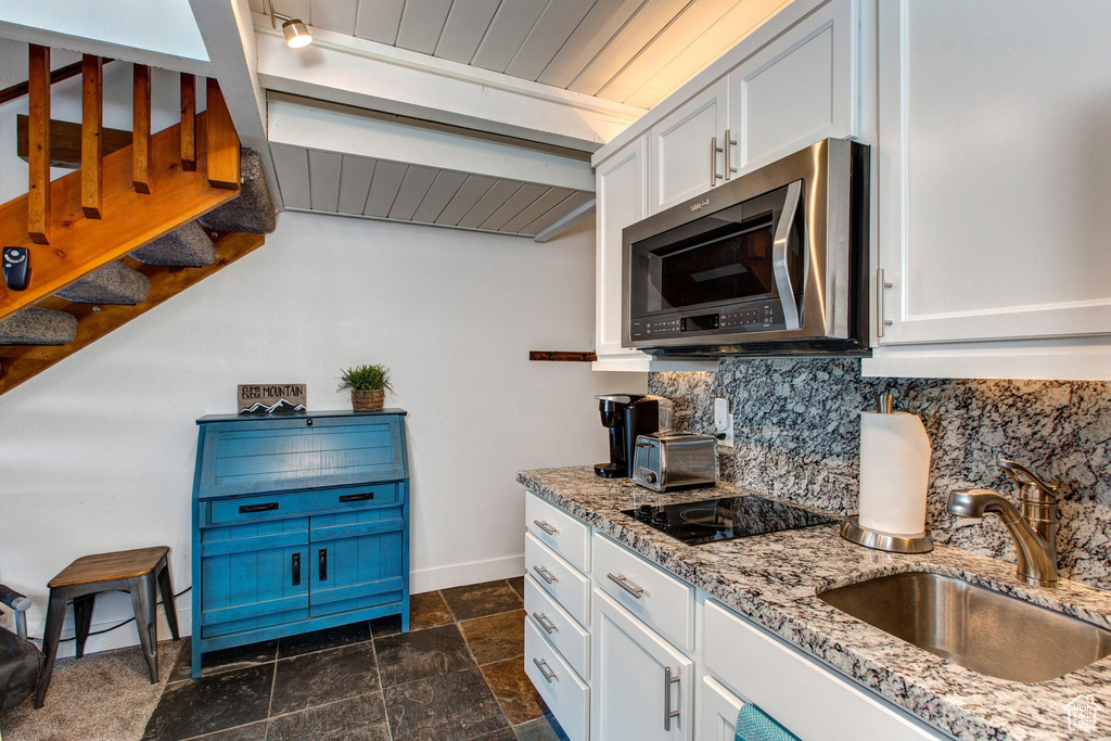 Kitchen with sink, white cabinetry, light stone counters, tasteful backsplash, and black electric cooktop
