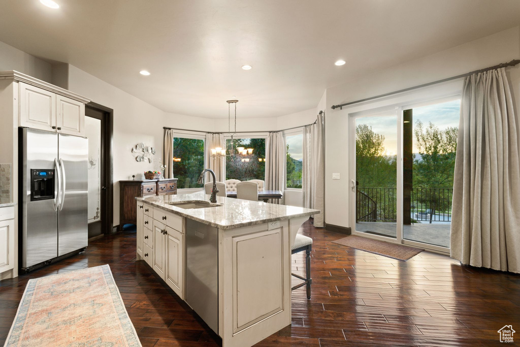 Kitchen featuring stainless steel appliances, a sink, light stone countertops, an island with sink, and dark wood-style flooring