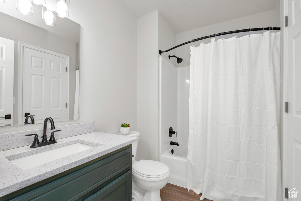 Full bathroom with hardwood / wood-style flooring, vanity, shower / bathtub combination with curtain, and toilet