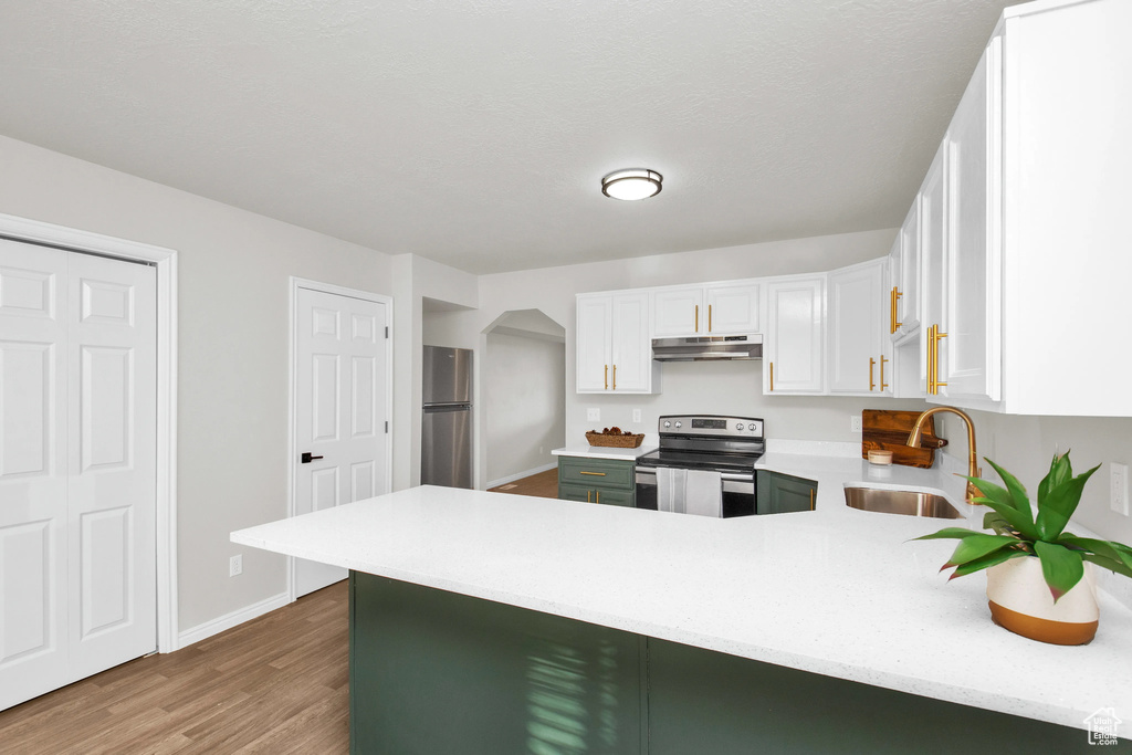 Kitchen featuring sink, white cabinetry, wood-type flooring, kitchen peninsula, and stainless steel appliances