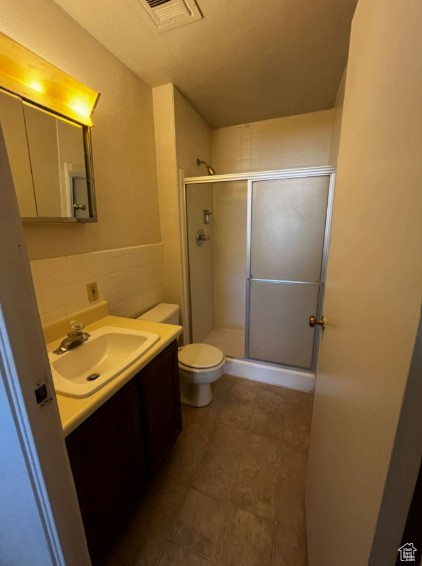 Bathroom with a shower with door, vanity, tile walls, and toilet