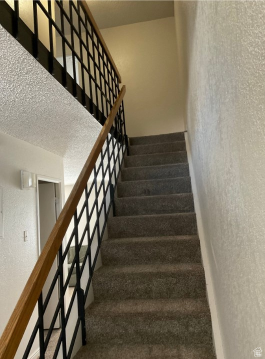 Stairs with carpet and a textured ceiling