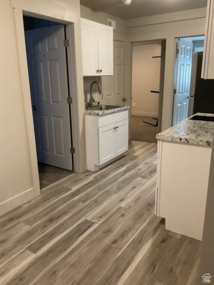 Kitchen featuring sink, white cabinetry, light hardwood / wood-style flooring, stainless steel refrigerator, and light stone countertops