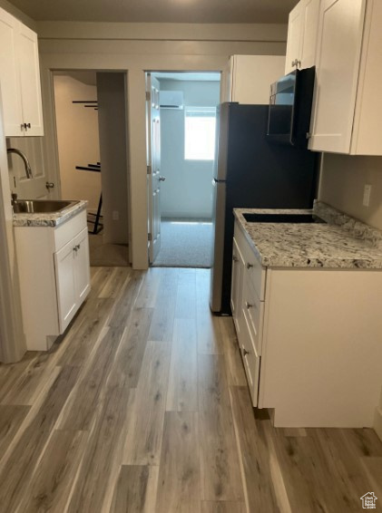 Kitchen featuring sink, white cabinetry, light stone counters, a baseboard radiator, and light hardwood / wood-style floors