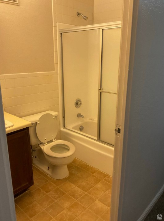 Full bathroom featuring vanity, tile walls, shower / bath combination with glass door, and toilet