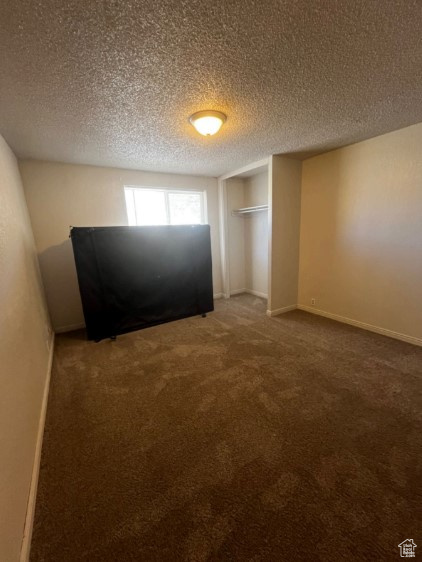 Unfurnished bedroom with a closet, a textured ceiling, and dark colored carpet