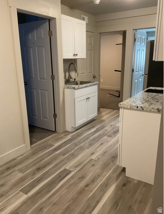 Kitchen with sink, light hardwood / wood-style flooring, stainless steel fridge, light stone countertops, and white cabinets
