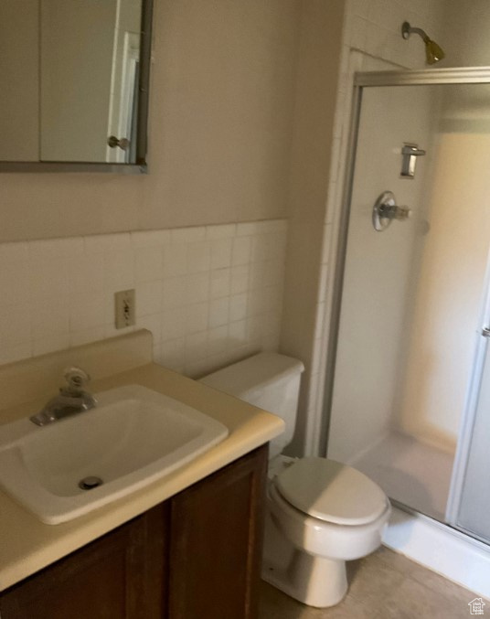 Bathroom with a shower with shower door, backsplash, vanity, toilet, and tile patterned floors