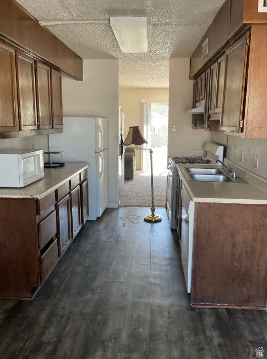 Kitchen with sink, white appliances, and dark colored carpet