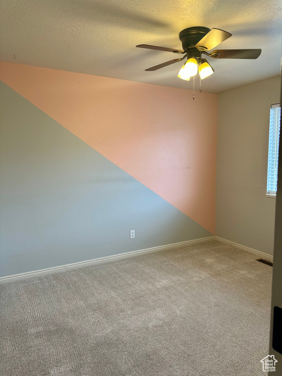 Empty room with ceiling fan, a textured ceiling, and carpet