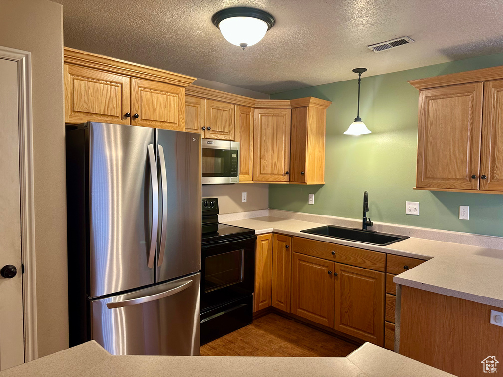 Kitchen featuring appliances with stainless steel finishes, decorative light fixtures, sink, and a textured ceiling