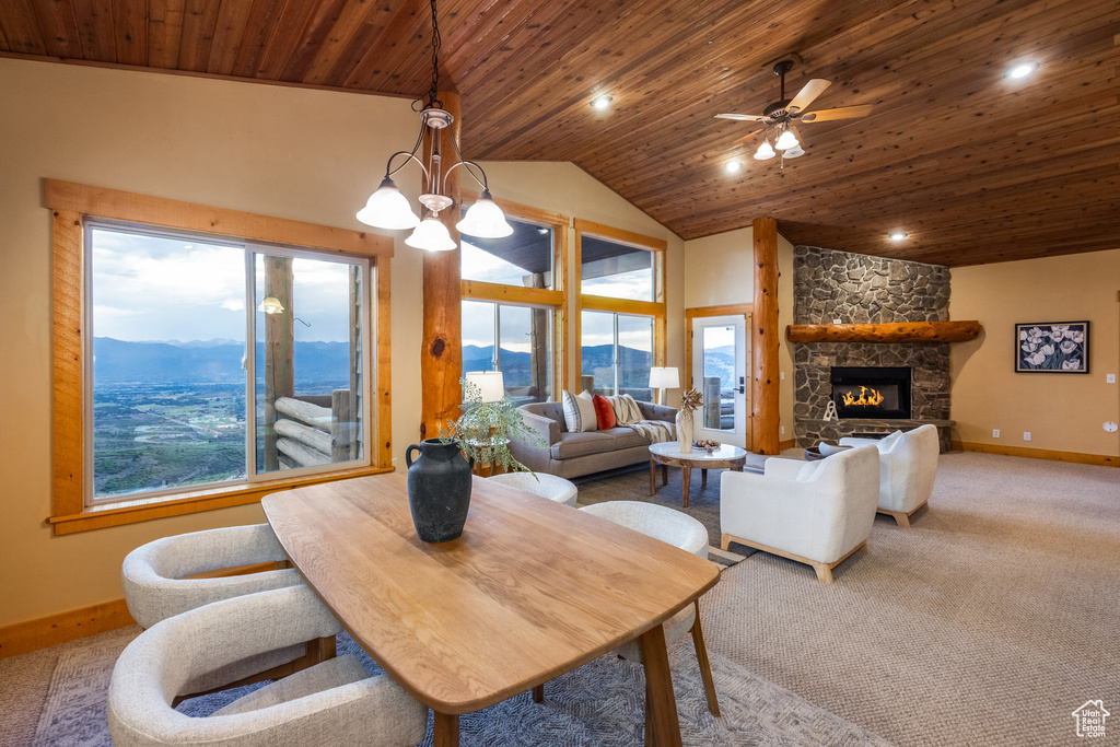 Carpeted dining space featuring wood ceiling, a mountain view, lofted ceiling, ceiling fan, and a stone fireplace