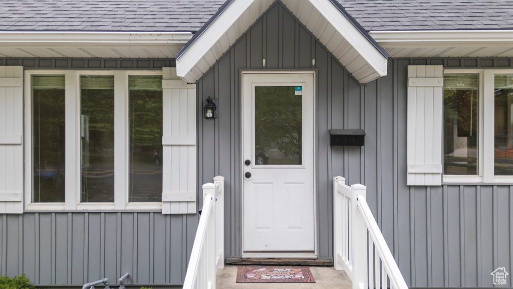 Doorway to property with board and batten siding and roof with shingles