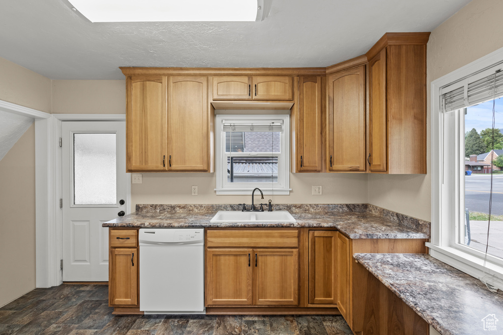 Kitchen with white dishwasher, a sink, stone finish flooring, and brown cabinets