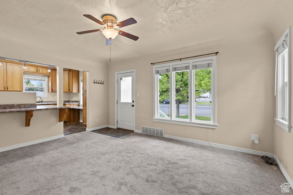 Kitchen featuring dark carpet, a ceiling fan, a kitchen breakfast bar, a sink, and a textured ceiling