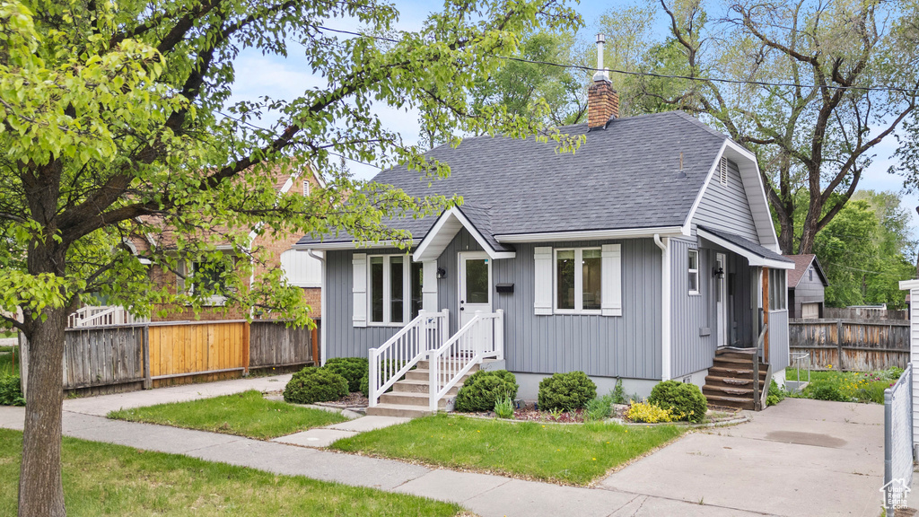 Bungalow-style house featuring roof with shingles and a chimney