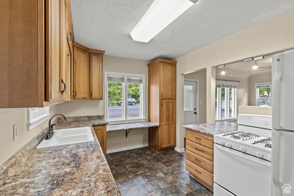 Kitchen featuring white appliances, a sink, healthy amount of natural light, dark stone finish floors, and a textured ceiling